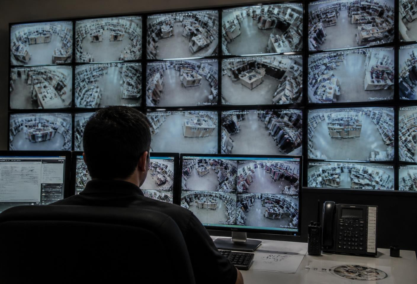 Operator monitoring a wall of CCTV screens showing retail camera feeds